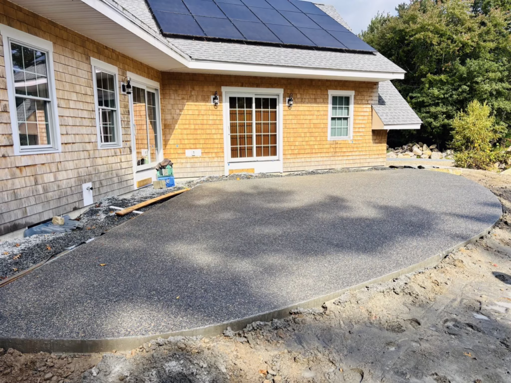Exposed aggregate concrete patio behind a cedar-shingled home